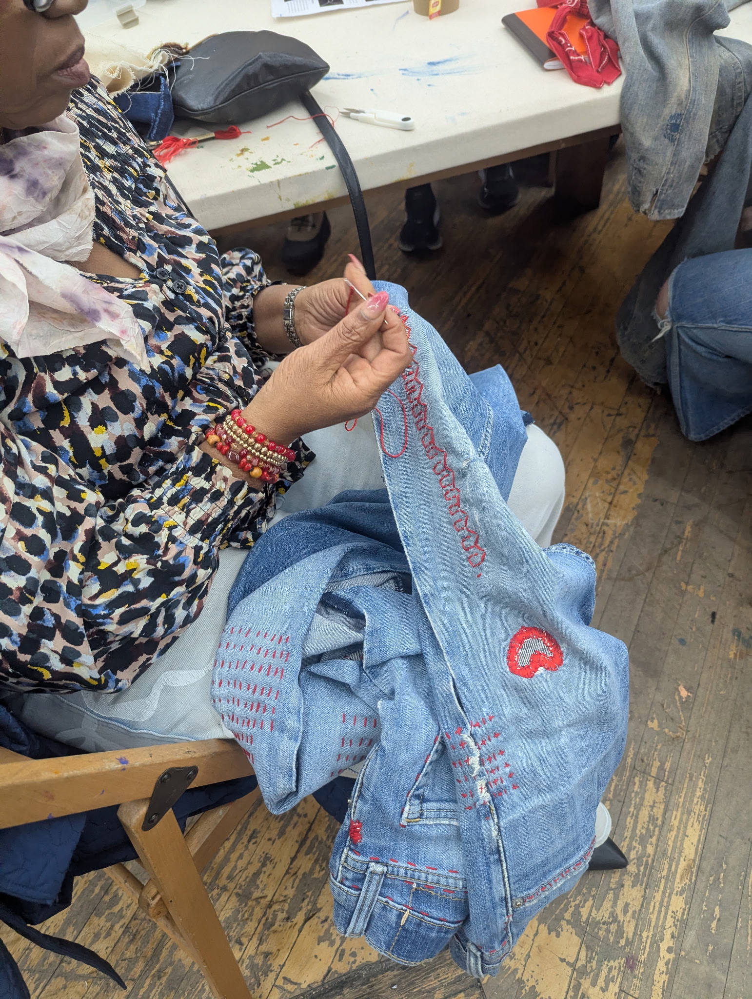 A woman repairs demin with bright red thread
