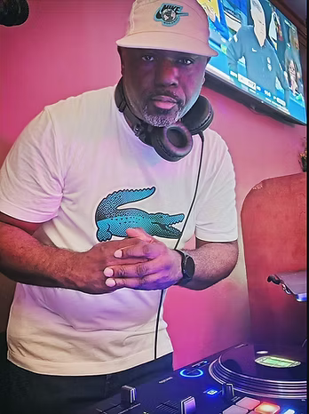 DJ RAH EASTWOOD Black man in a white tee shirt standing next to turntables