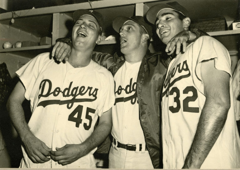 Black and white photograph of three Dodgers players in locker room.