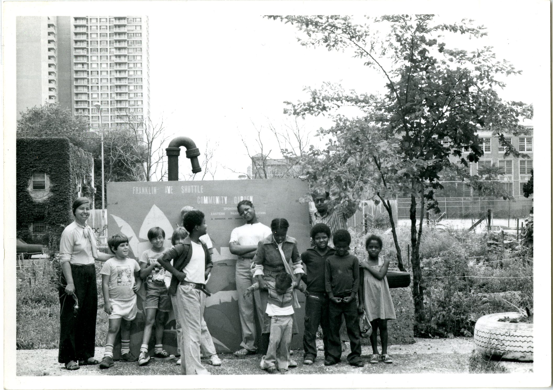 group of children and one adult in front of garden