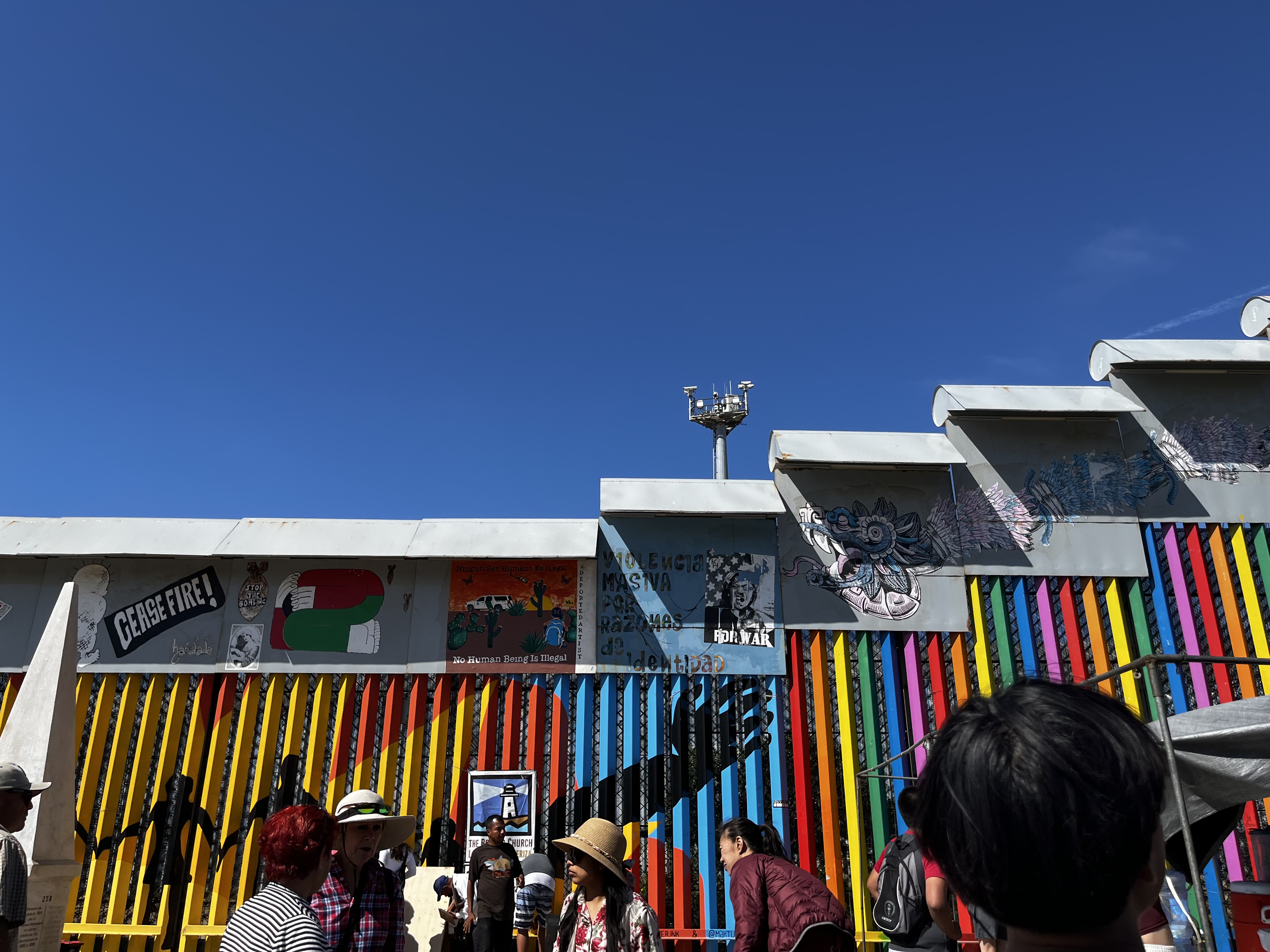 Political messages and murals cover the border wall on the Tijuana side, including the words "No Human Being Is Illegal" beneath a surveillance tower.