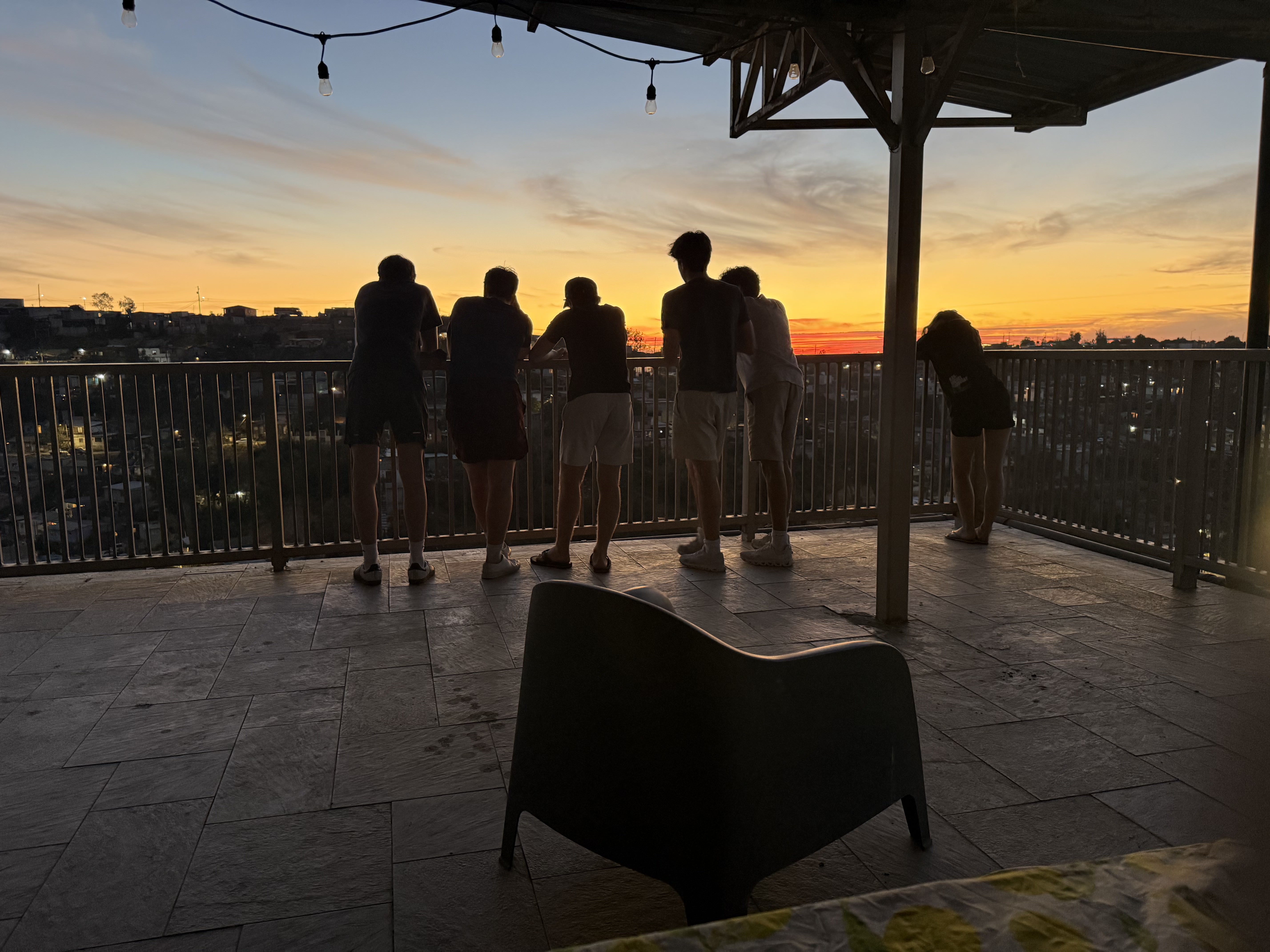 A group of students watch the sunset over the Tijuana skyline from a rooftop terrace.