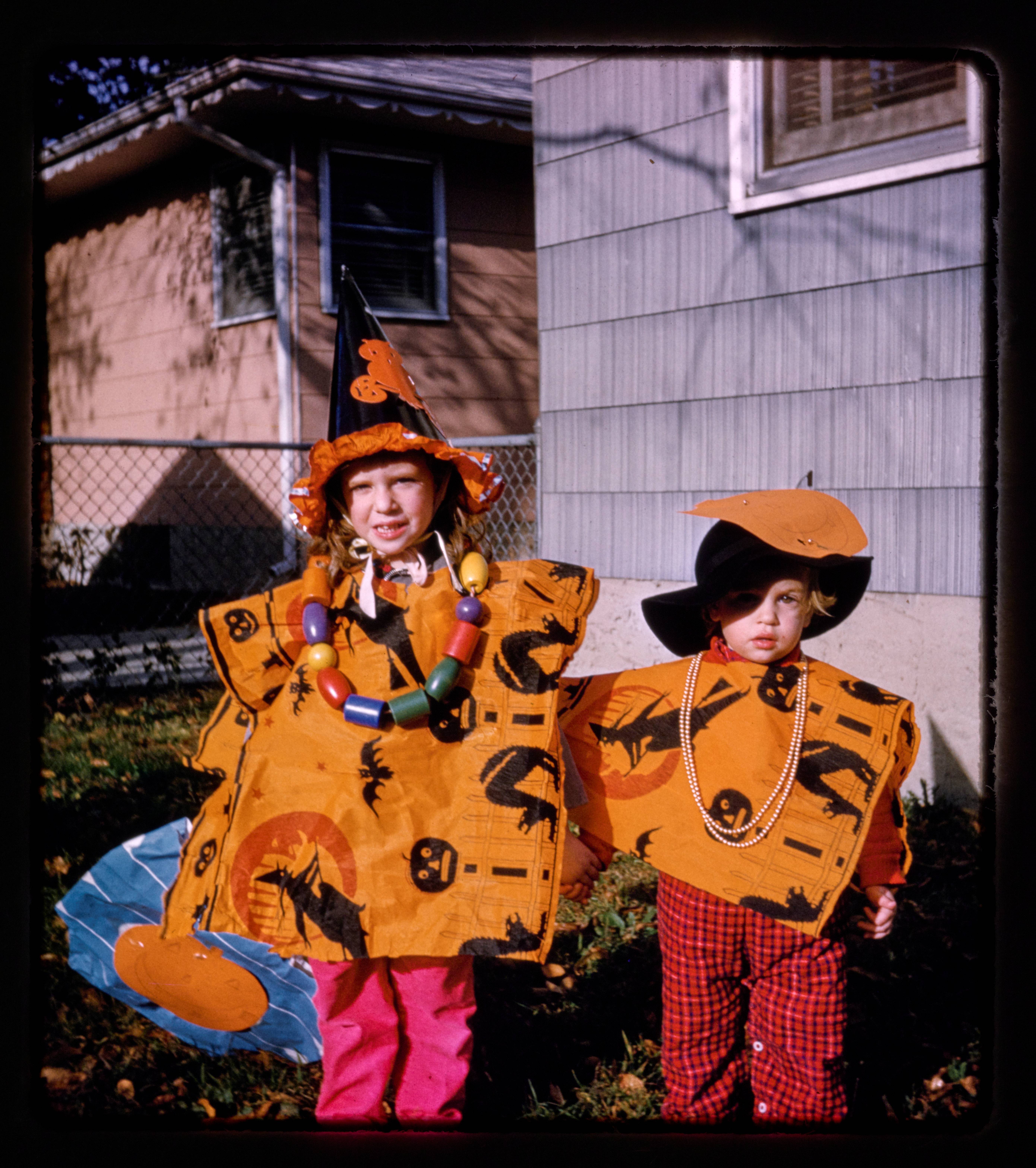 Two childrenin orange Halloween costumes standing in the backyard of a house.