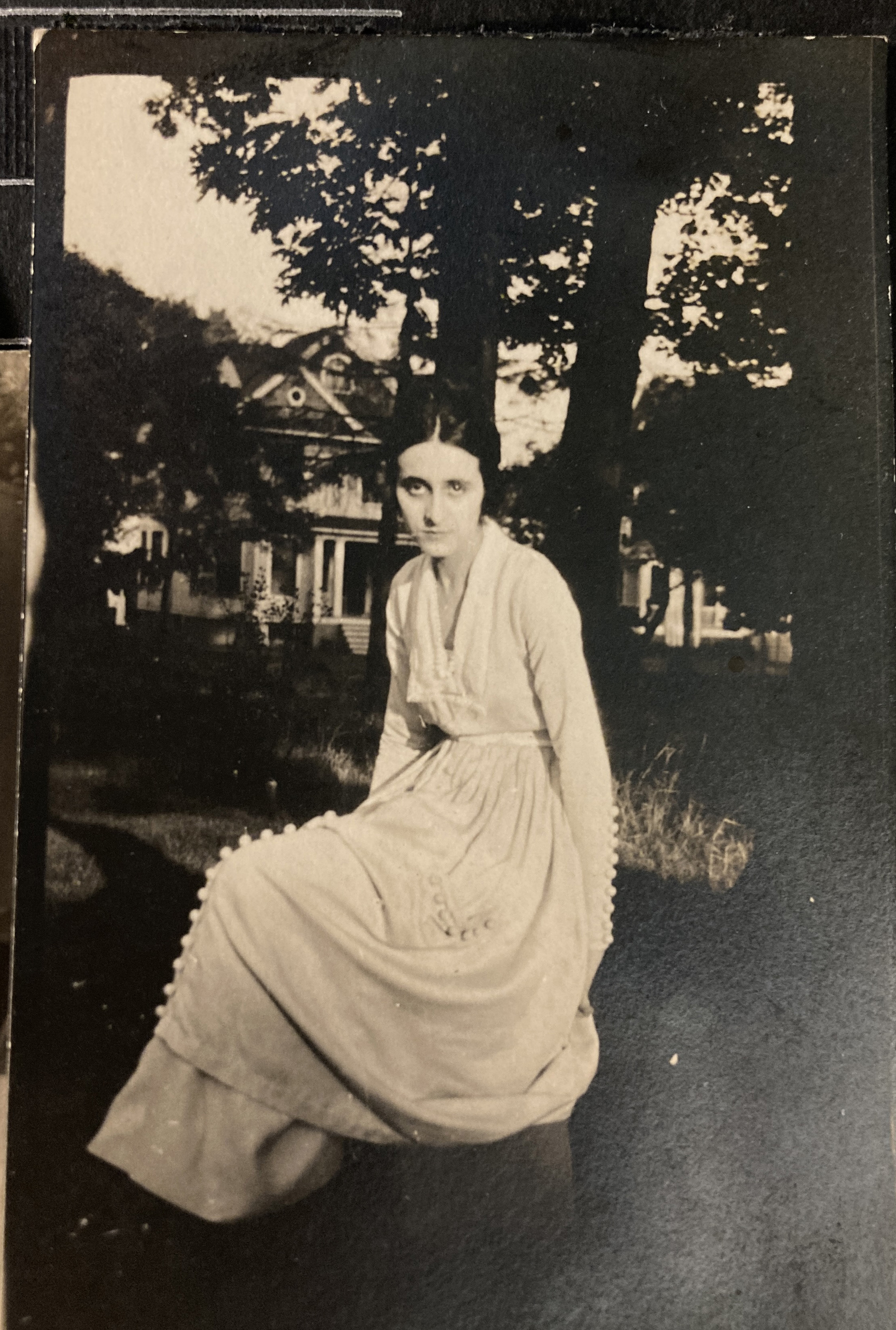 Young woman in long dress sitting in the wooded area in front of house. 