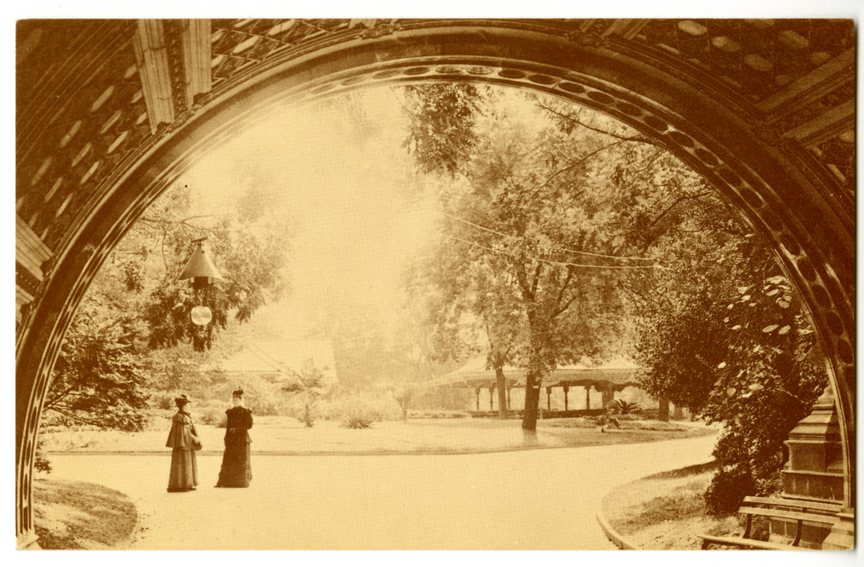 Sepia photographic postcard of two Victorian women stand outside the Cleft Ridge Span tunnel with Concert Grove in the distance.