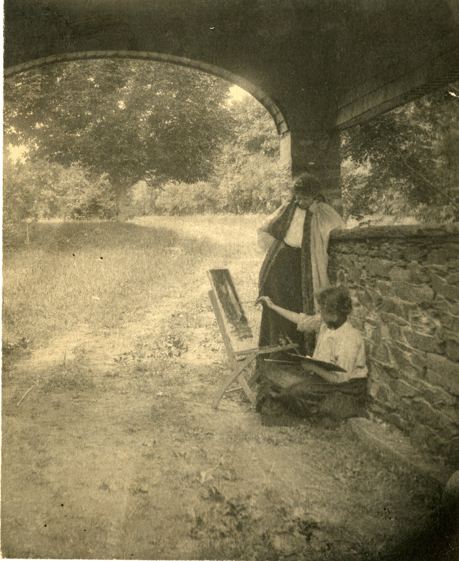 Black and white photograph of two young women under an archway with trees behind