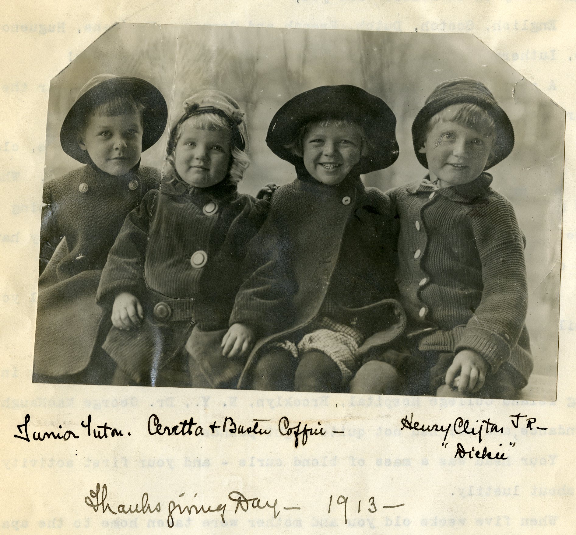 Black and white photograph of four small children seated in a row in hats and coats