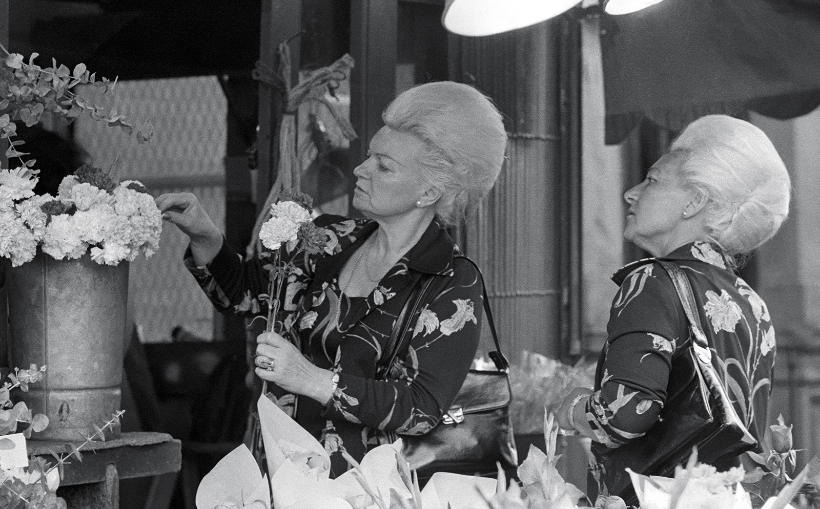 Twins in flowered blouses choosing flowers in a shop