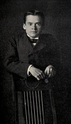 Black and white photographic portrait of Paul Leicester Ford standing behind a chair back.
