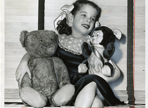 black-and-white photograph of child in center holding two teddy bears in each arm