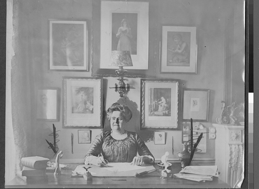 person sitting at desk with framed works of art in background