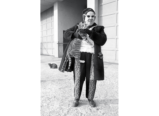 Older woman wearing black and leopard patterned outfit holding a cat in her arms.
