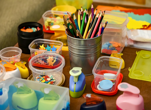 Colored pencils and various small containers containing craft supplies are laid out on a wooden table.