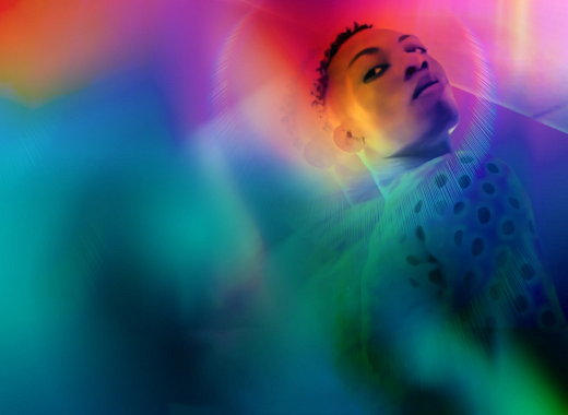 a queer Nigerian stands defiantly bathed in a cascading rainbow overlay
