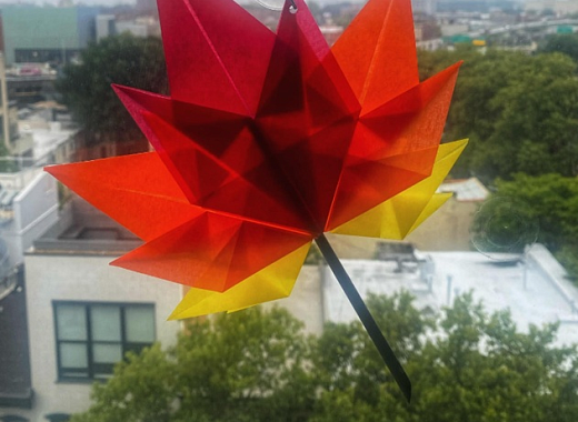 red, orange, yellow origami leaf against a city backdrop.